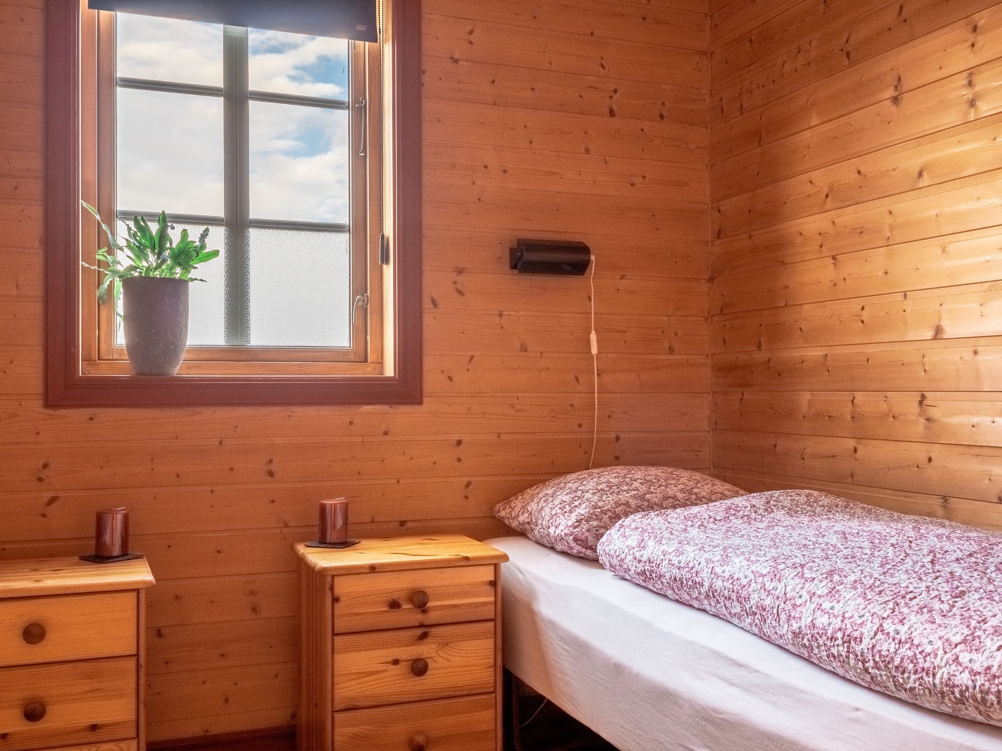 Bedroom with wooden panelling, a single bed, and a window with a plant on the sill