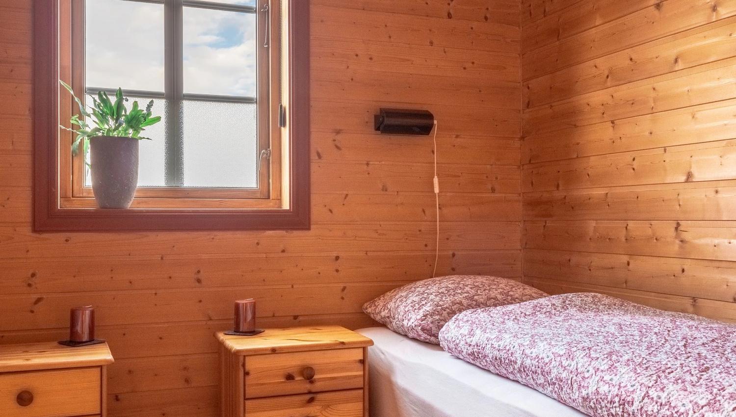 Bedroom with wooden panelling, a single bed, and a window with a plant on the sill