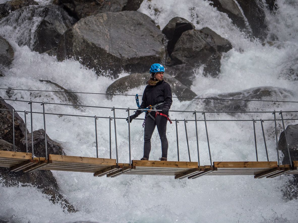 Brevandrar krysser ei hengebru over kraftig smeltevatn frå breen.
