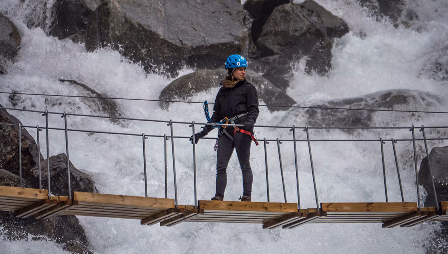 Brevandrar krysser ei hengebru over kraftig smeltevatn frå breen.