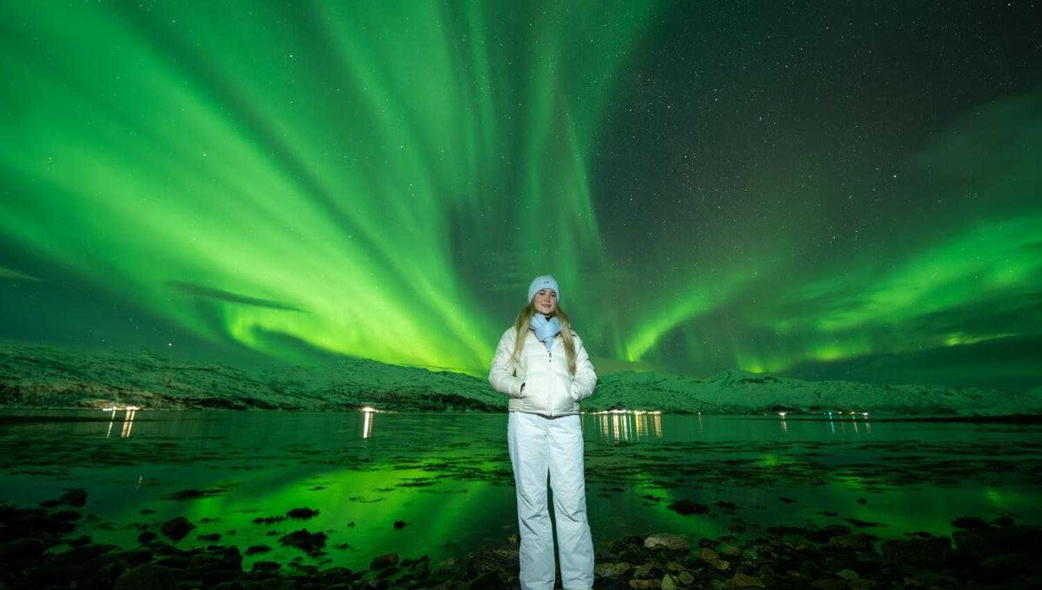 A guest poses in front of a Northern Lights show covering the whole sky