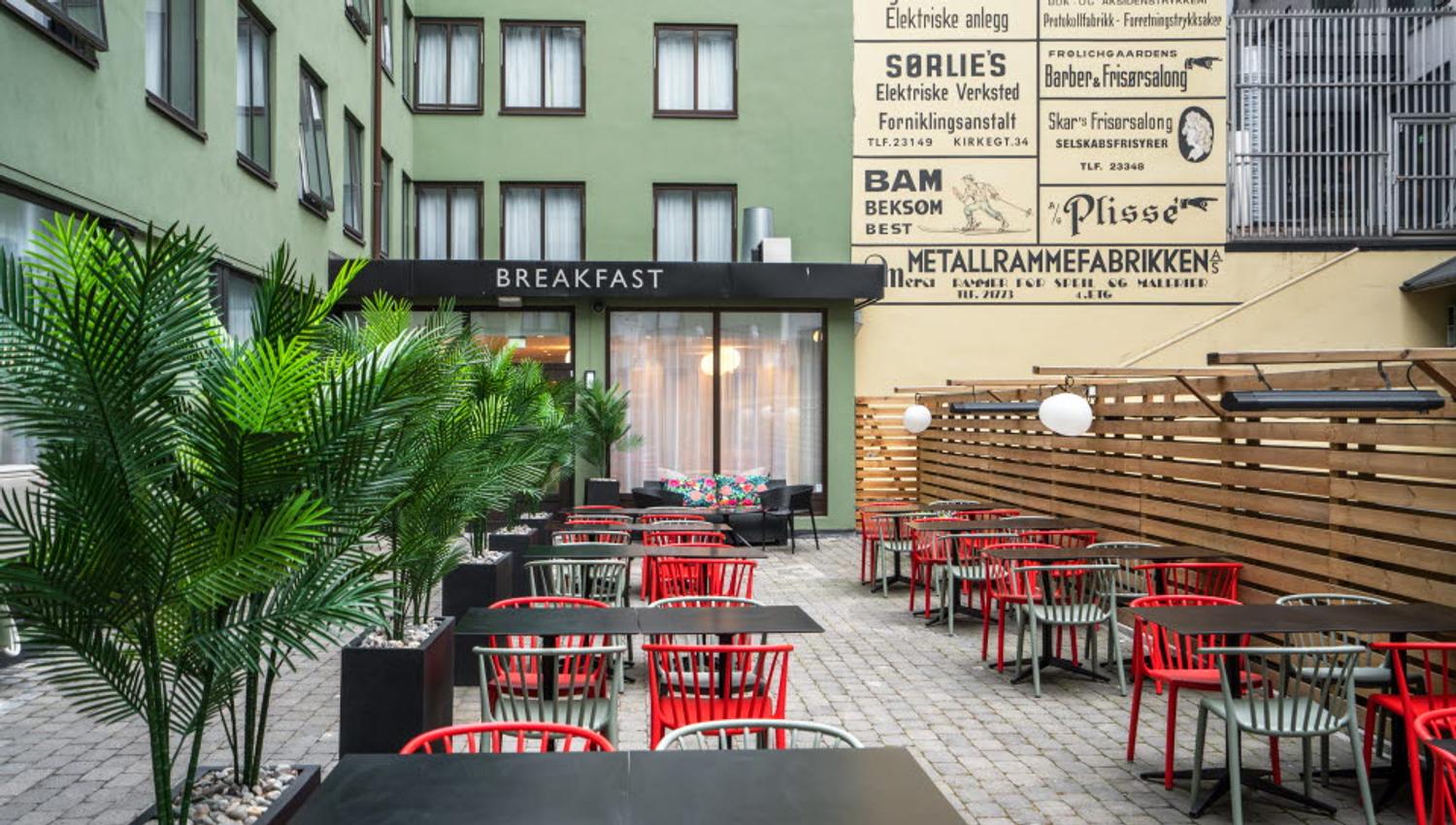 Bakgård med sorte bord, røde stoler og store pottplanter.