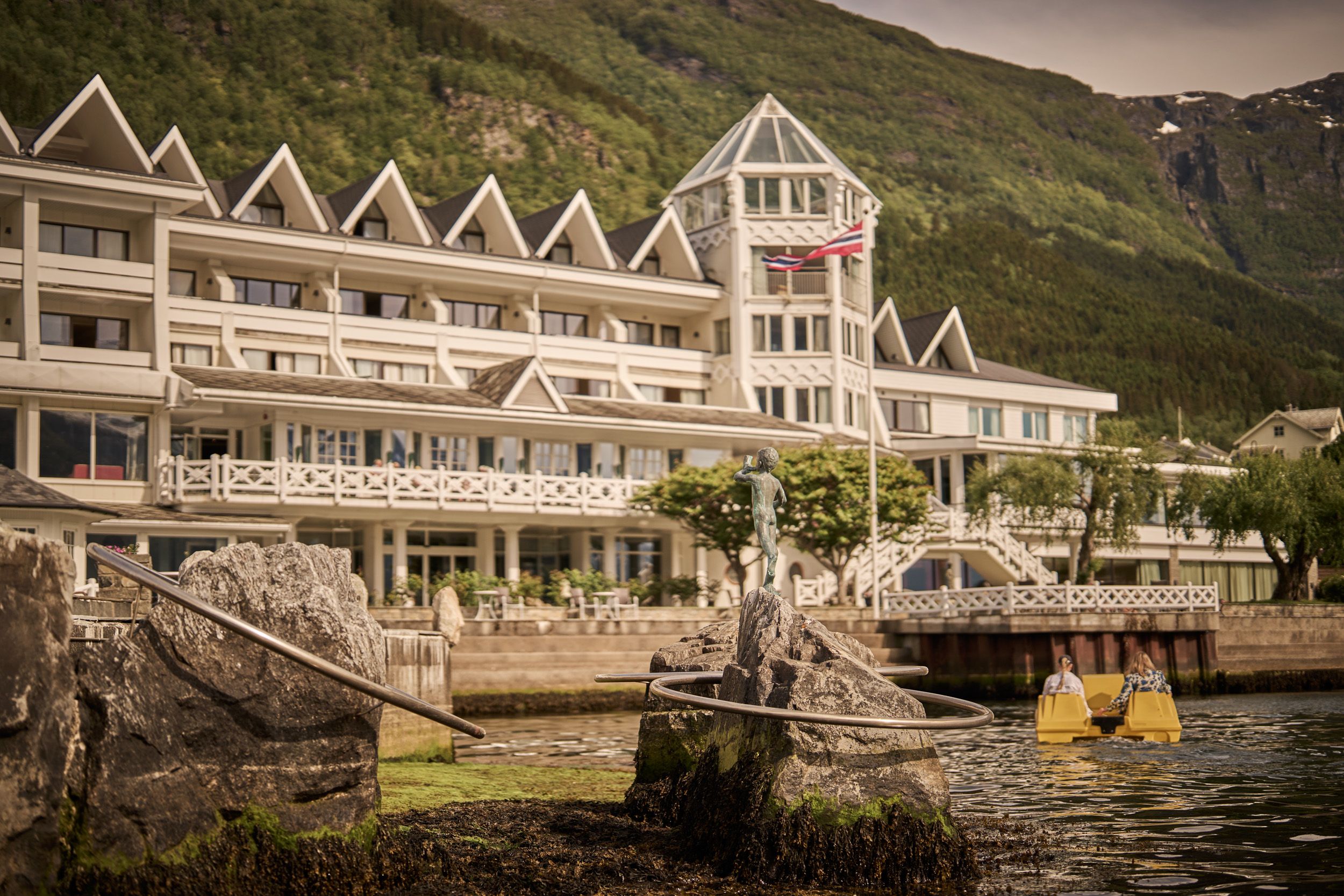 Guests enjoying a pedal boat ride with Hotel Ullensvang and the mountain backdrop.