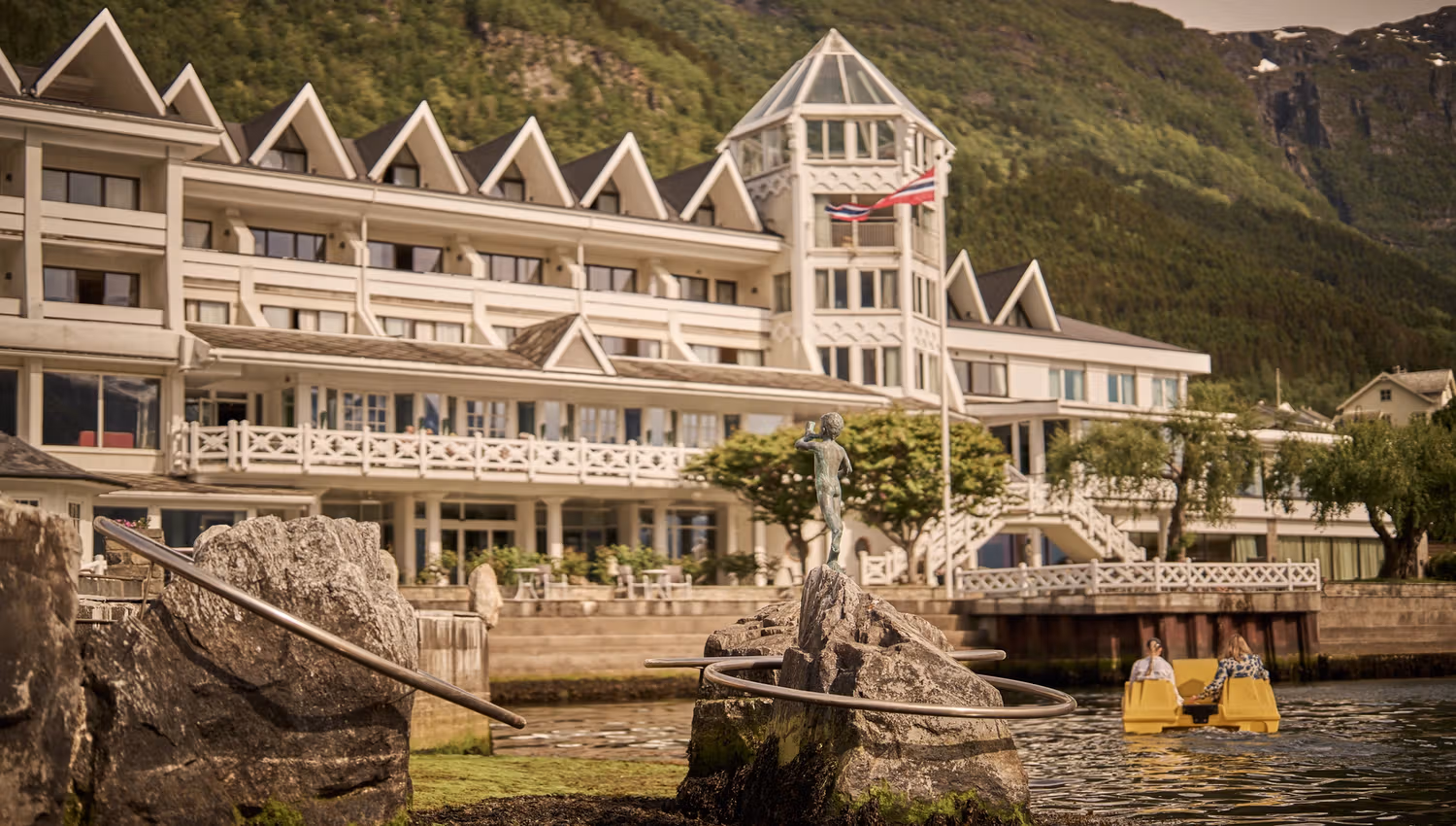 Guests enjoying a pedal boat ride with Hotel Ullensvang and the mountain backdrop.