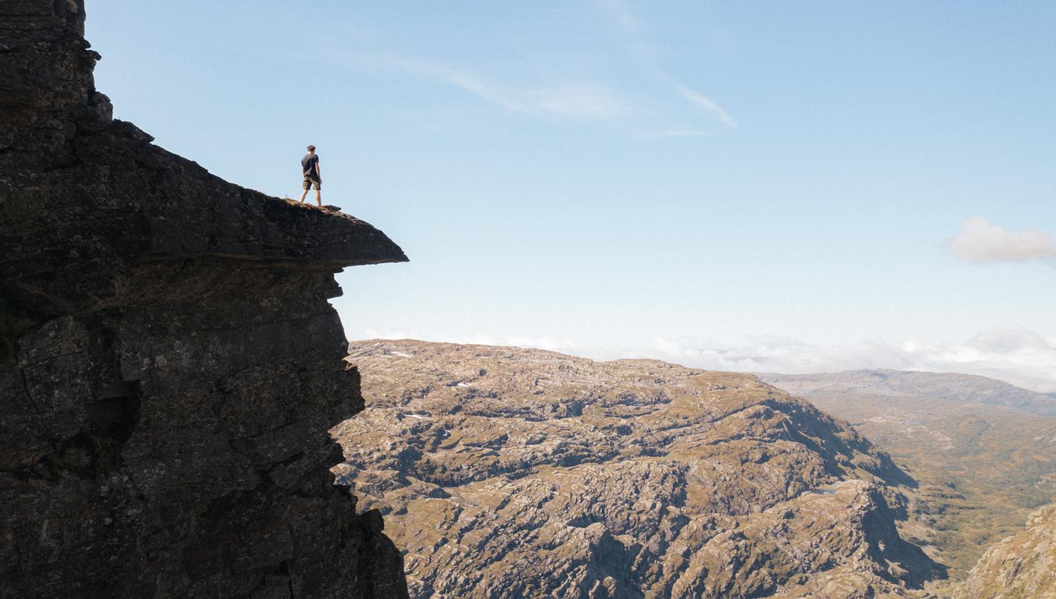 Person står på en massiv fjelltopp og ser utover fjellandskapet.