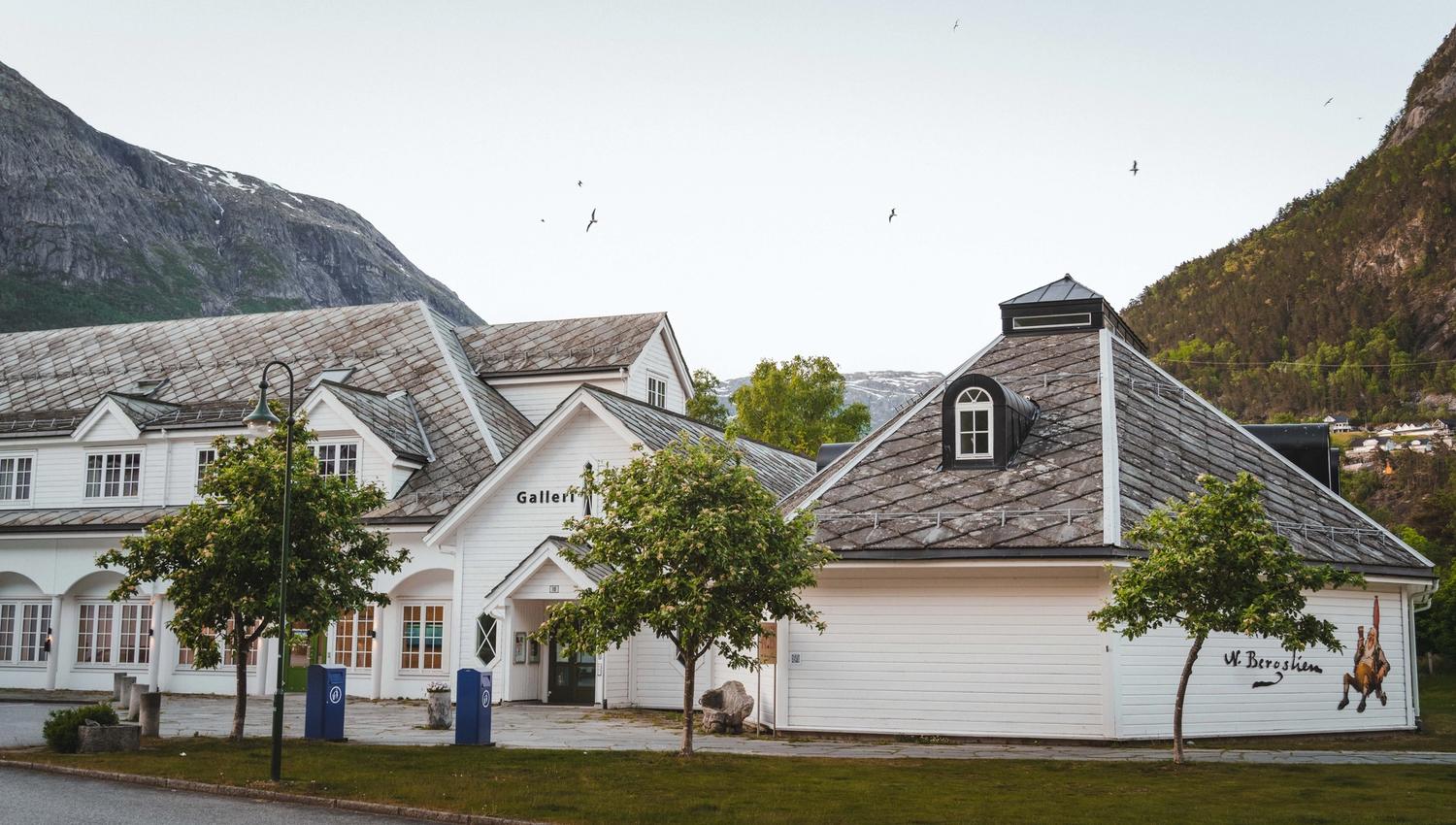 The gallery seen from the outside during sunset, a flock of birds flying in the sky.