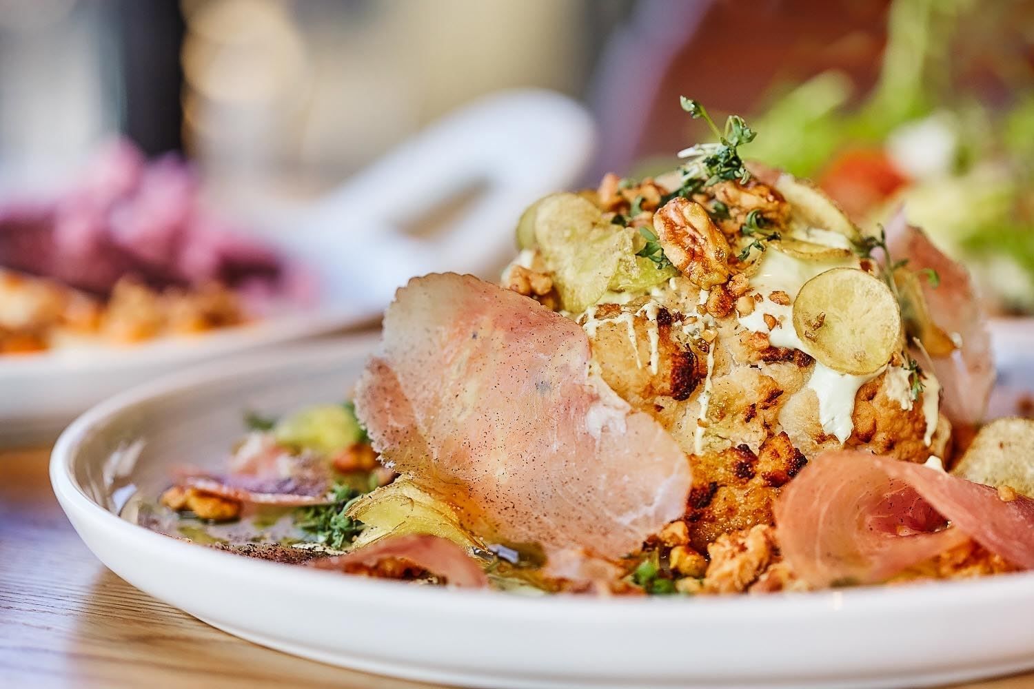 Close-up of a plated gourmet salad topped with walnuts, herbs, creamy dressing, and thin potato slices on a table..