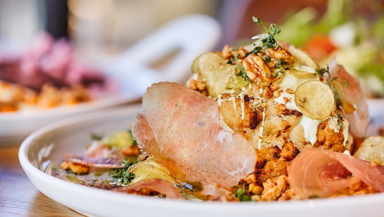 Close-up of a plated gourmet salad topped with walnuts, herbs, creamy dressing, and thin potato slices on a table..