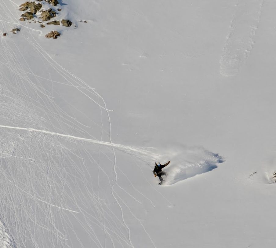 A person snowboarding down a mountain churning up snow during a turn