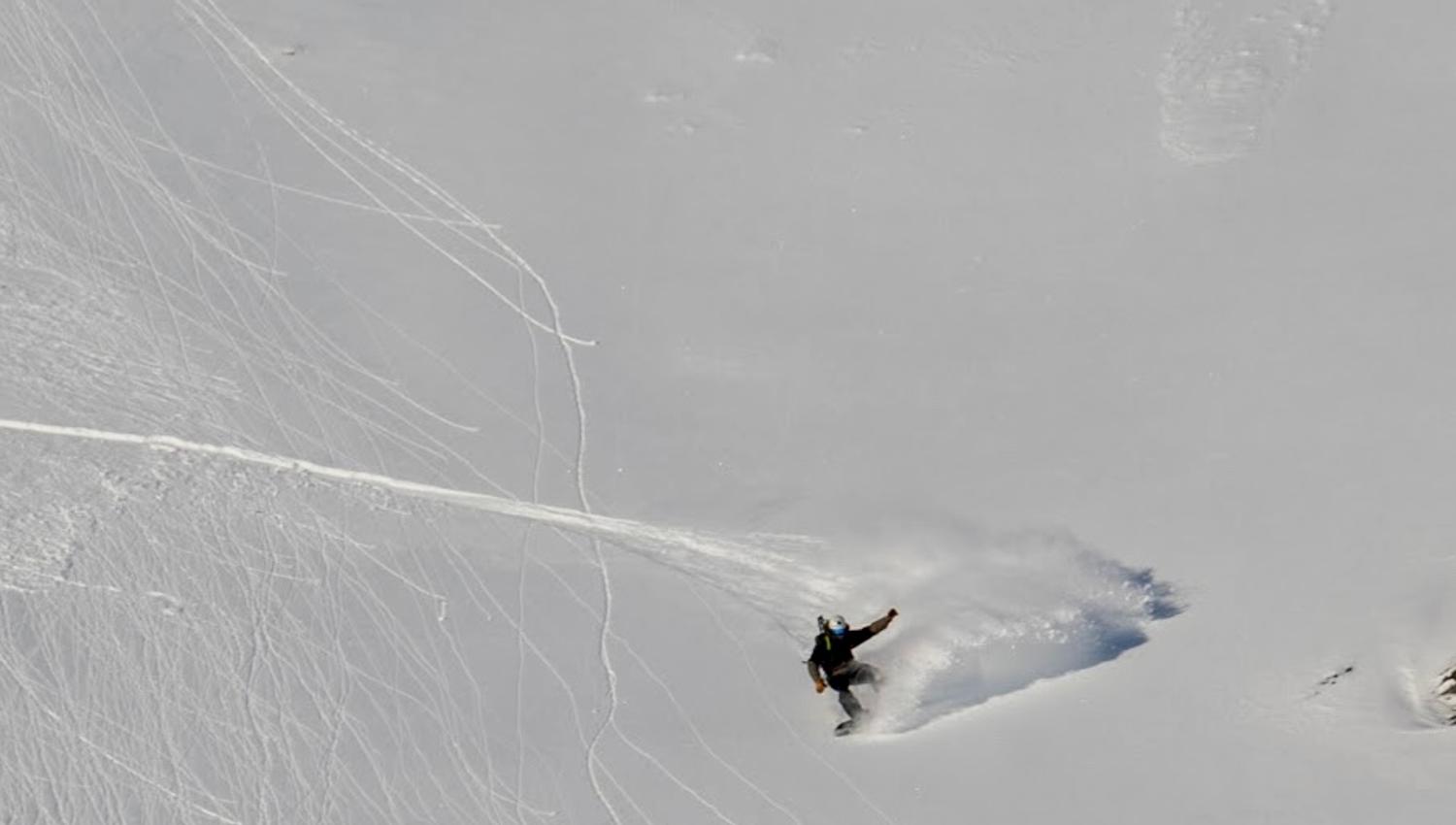 A person snowboarding down a mountain churning up snow during a turn