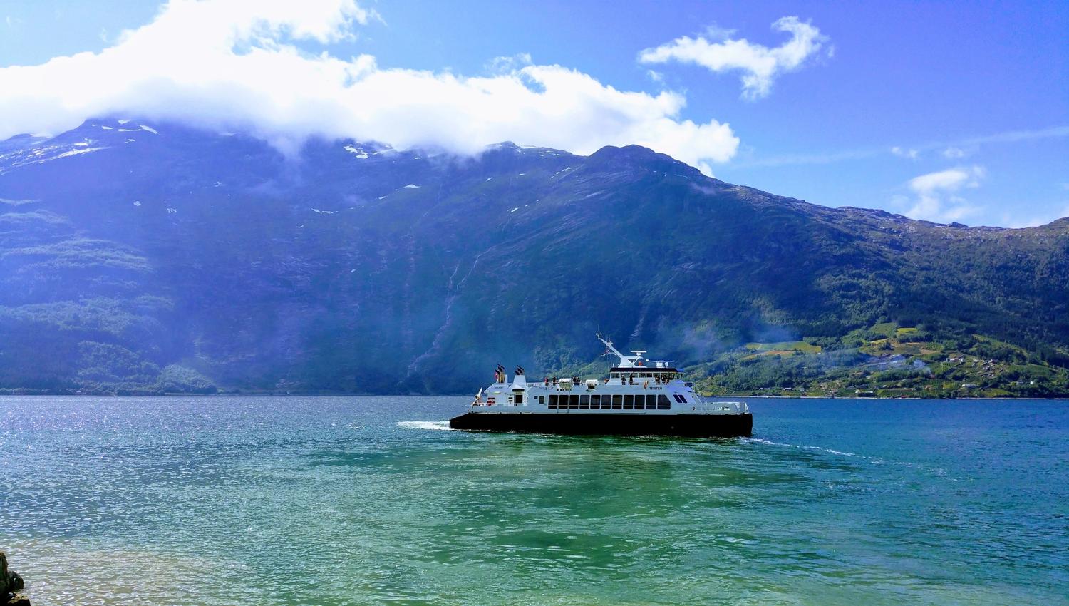 Ferry crossing the Hardangerfjord surrounded by majestic mountains and blue skies – an authentic travel experience in the heart of Hardanger.