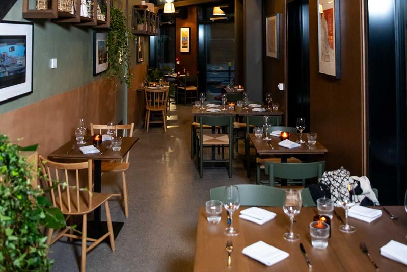 Restaurant interior with a high ceiling, small wooden tables set for dining and chairs