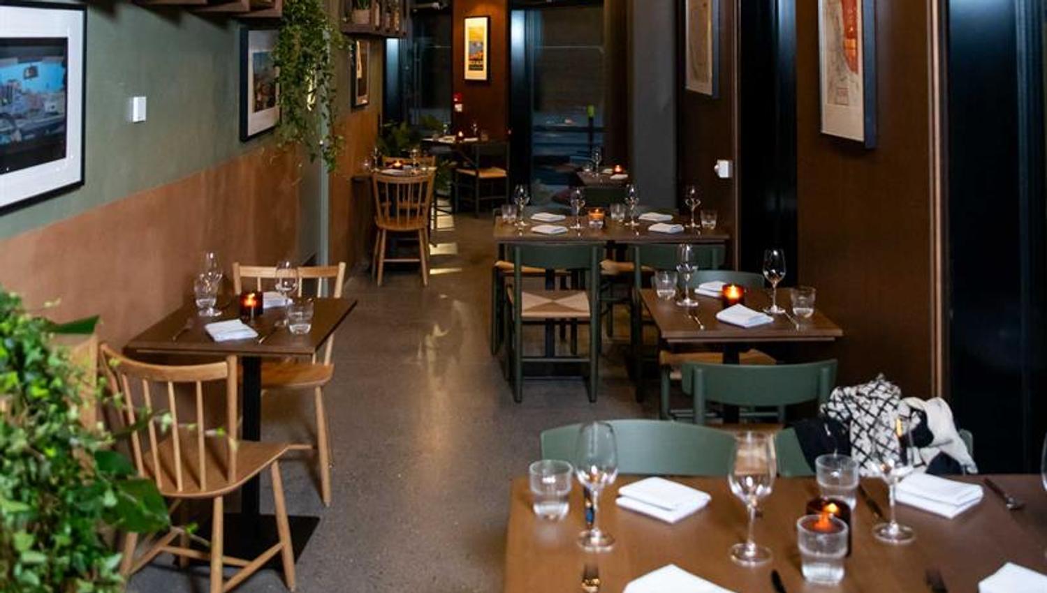 Restaurant interior with a high ceiling, small wooden tables set for dining and chairs