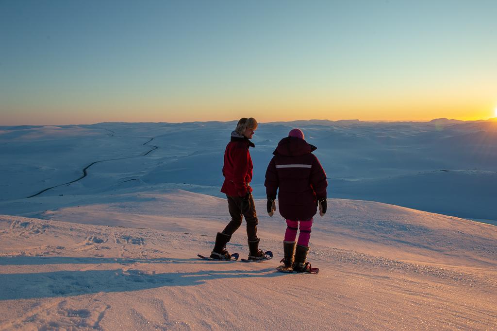 Two people on snowshoes on top of Halnekollen in a winter landscape at sunset.