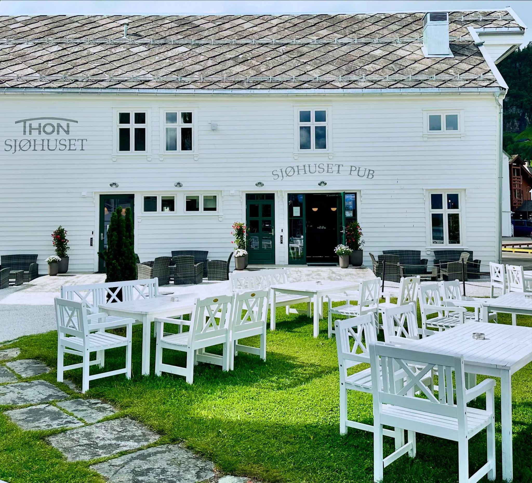 Sjøhuset's exterior, with its traditional Norwegian architecture reflecting in the calm waters of Norheimsund. Outdoor seating area visible with blank