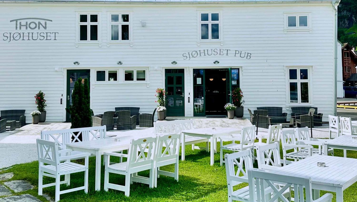 Sjøhuset's exterior, with its traditional Norwegian architecture reflecting in the calm waters of Norheimsund. Outdoor seating area visible with blank