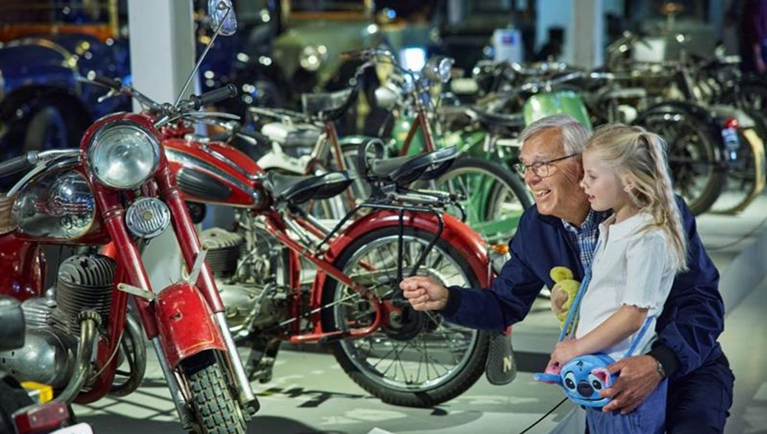 An elderly man and a little girl looking at motorcycles.