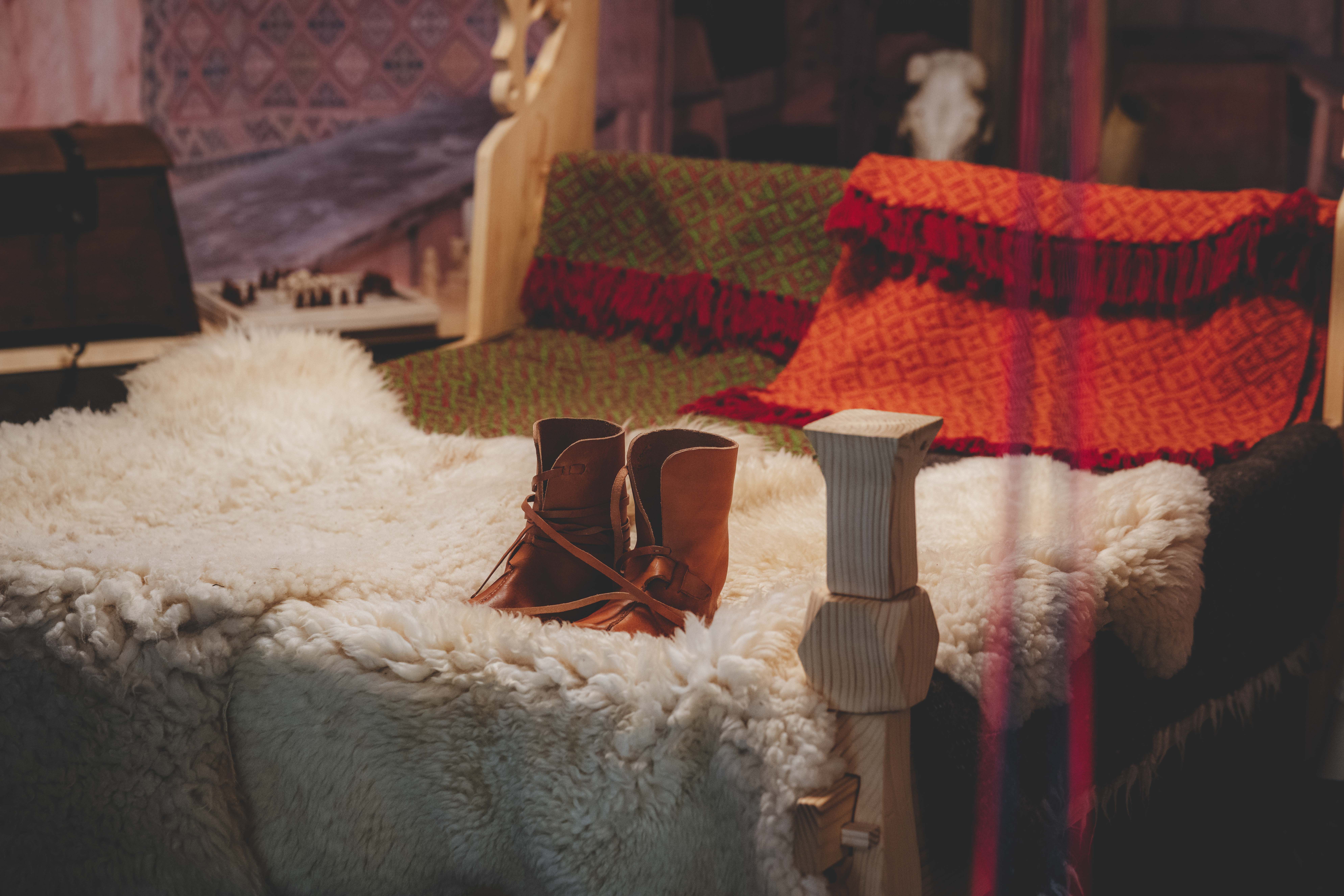 Ein Bett mit Schaffellen, gewebten Decken und einem Paar Lederschuhen auf der Schaffellen.
