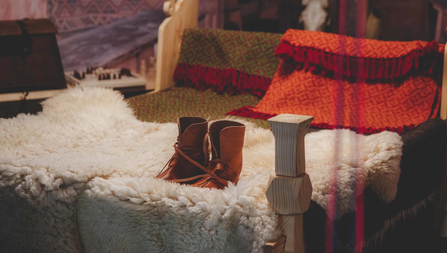 Ein Bett mit Schaffellen, gewebten Decken und einem Paar Lederschuhen auf der Schaffellen.