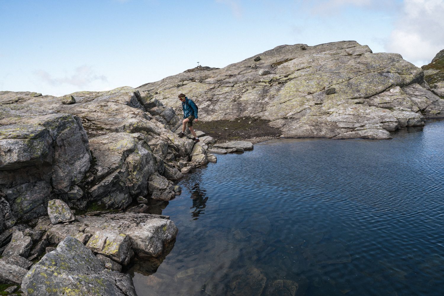 Person vandrer langs med eit vatn i fjellet.