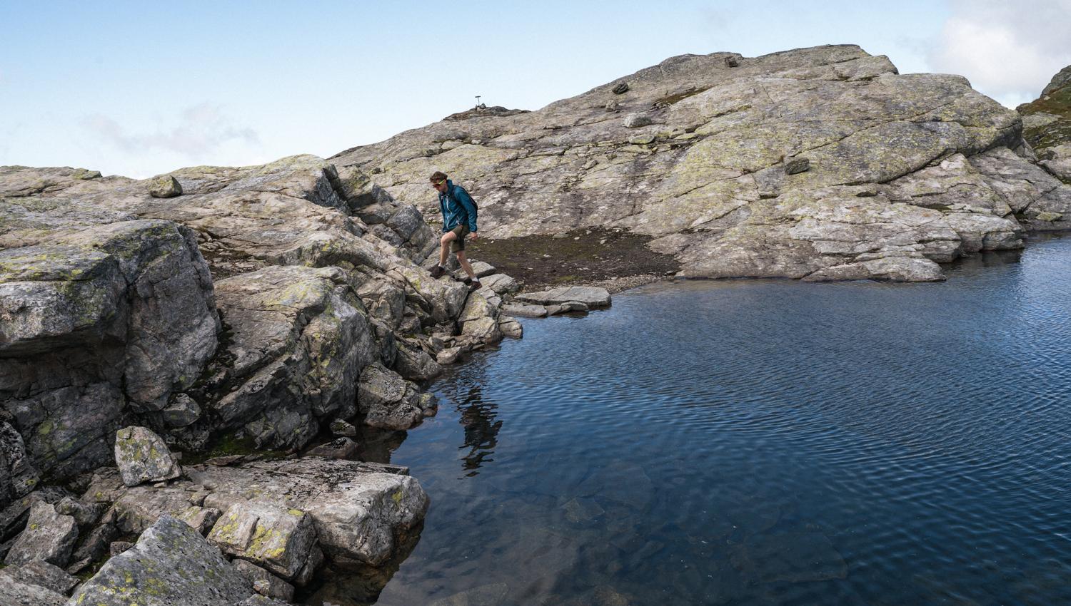 Person vandrer langs med eit vatn i fjellet.
