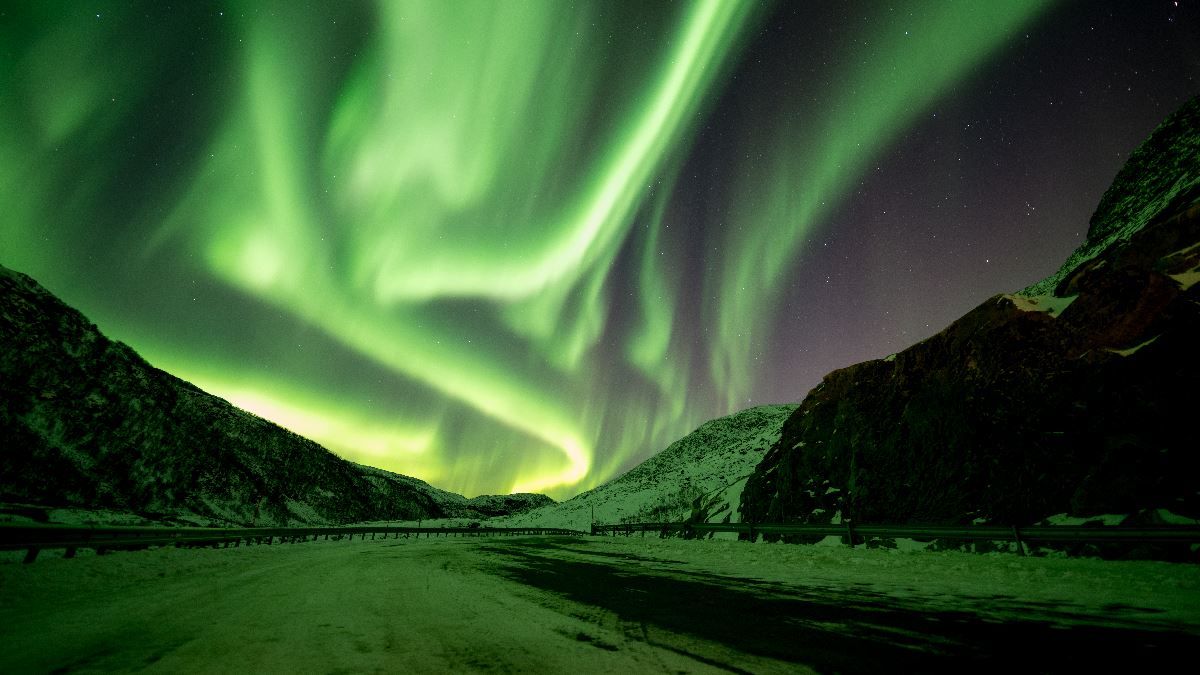Green Northern Lights illuminate the mountains and winter landscape outside Tromsø in Northern Norway.