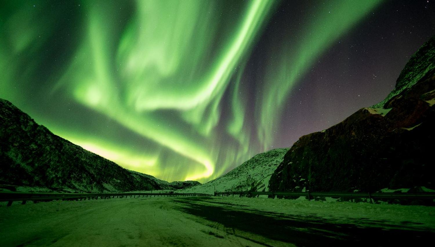 Green Northern Lights illuminate the mountains and winter landscape outside Tromsø in Northern Norway.