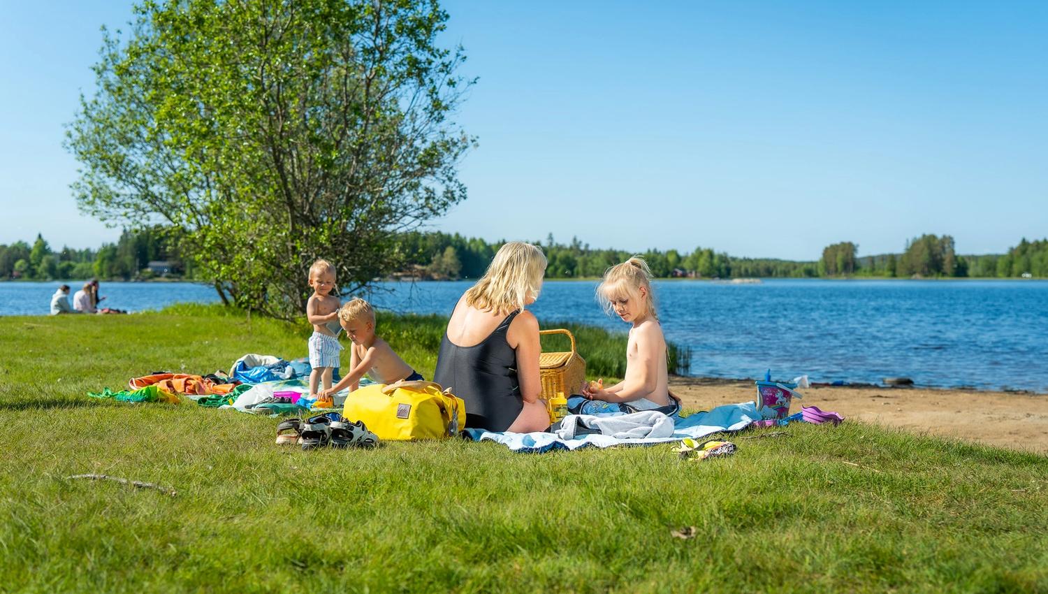 Barn og voksne som koser seg på gresset på Lundebyvannet