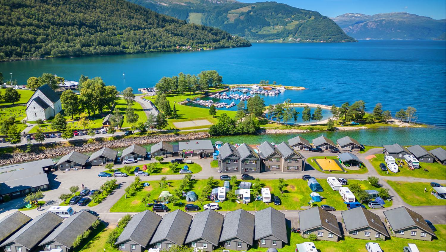 Luftaufnahme von Mikkelparken Ferietun in Kinsarvik, umgeben vom Hardangerfjord und majestätischen Bergen. Ein perfektes Urlaubsziel für die ganze Familie.