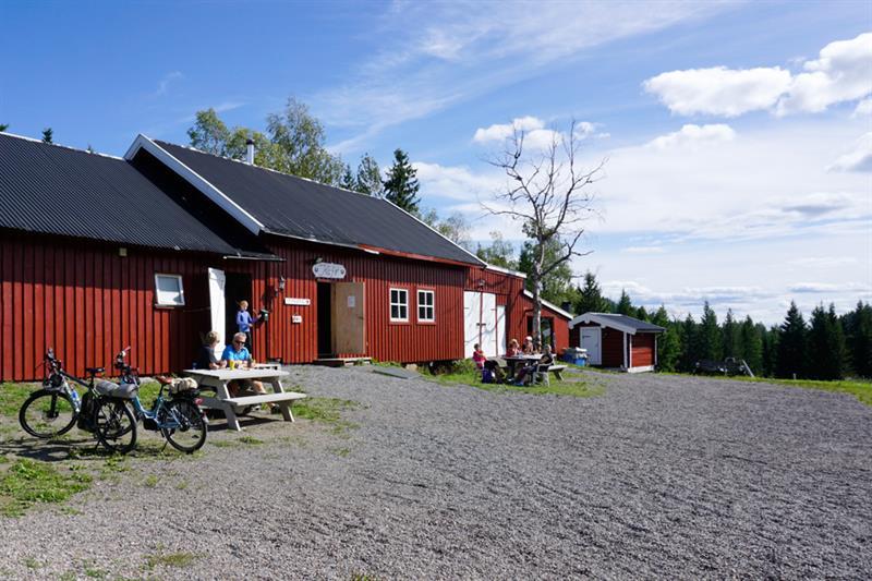 A red house by the forest with a couple of people sitting outside.
