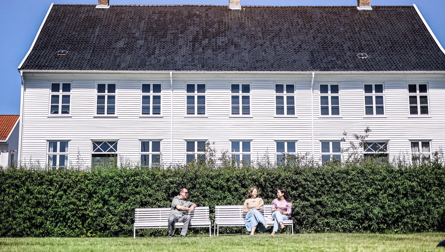 Two white benches in front of the museum with three people.