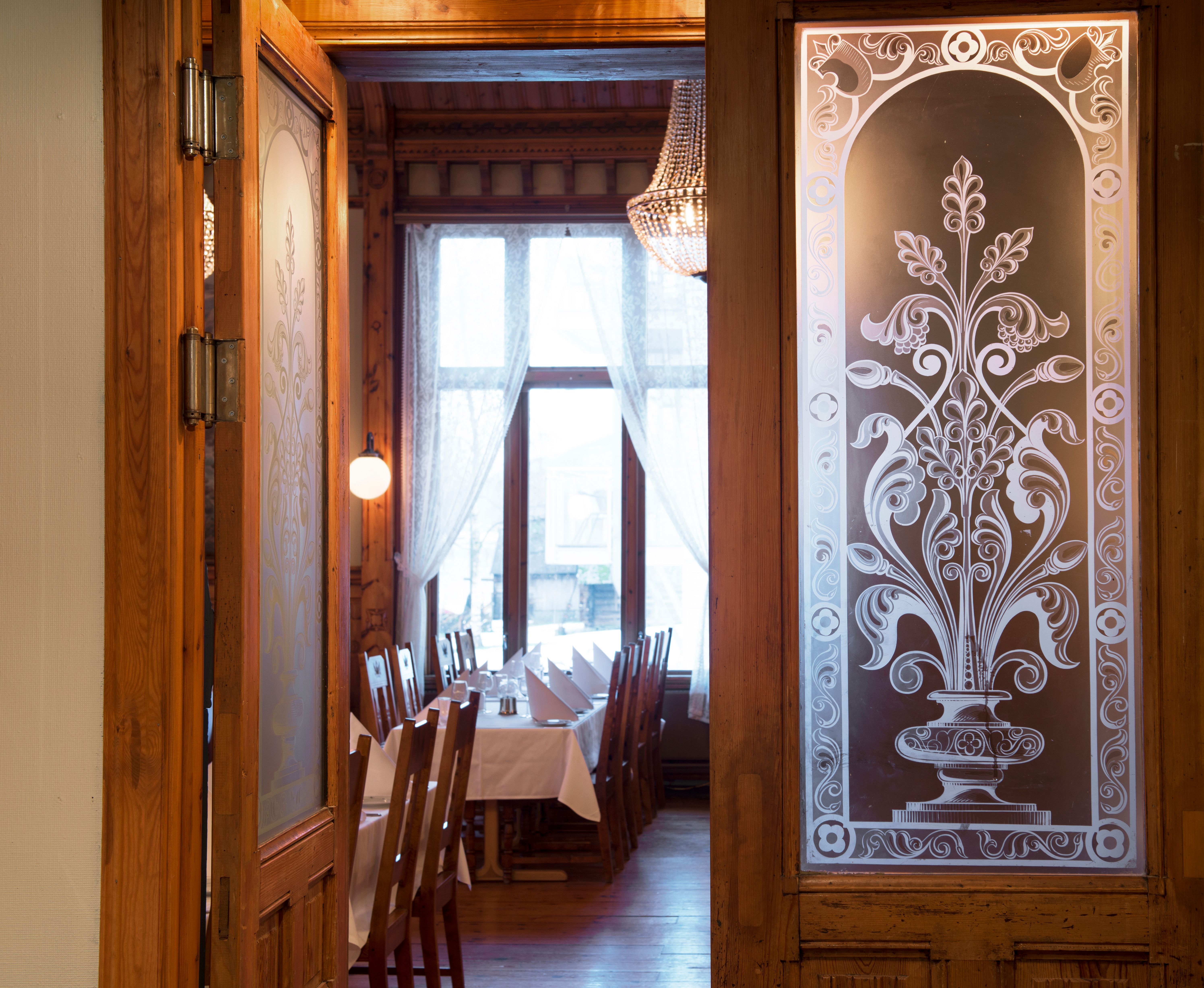 Atmospheric entrance to the restaurant at Thon Hotel Sandven, featuring classic carvings and glass details.