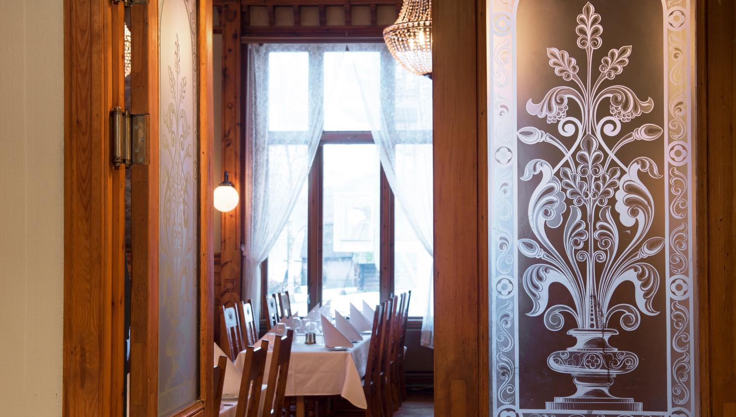 Atmospheric entrance to the restaurant at Thon Hotel Sandven, featuring classic carvings and glass details.