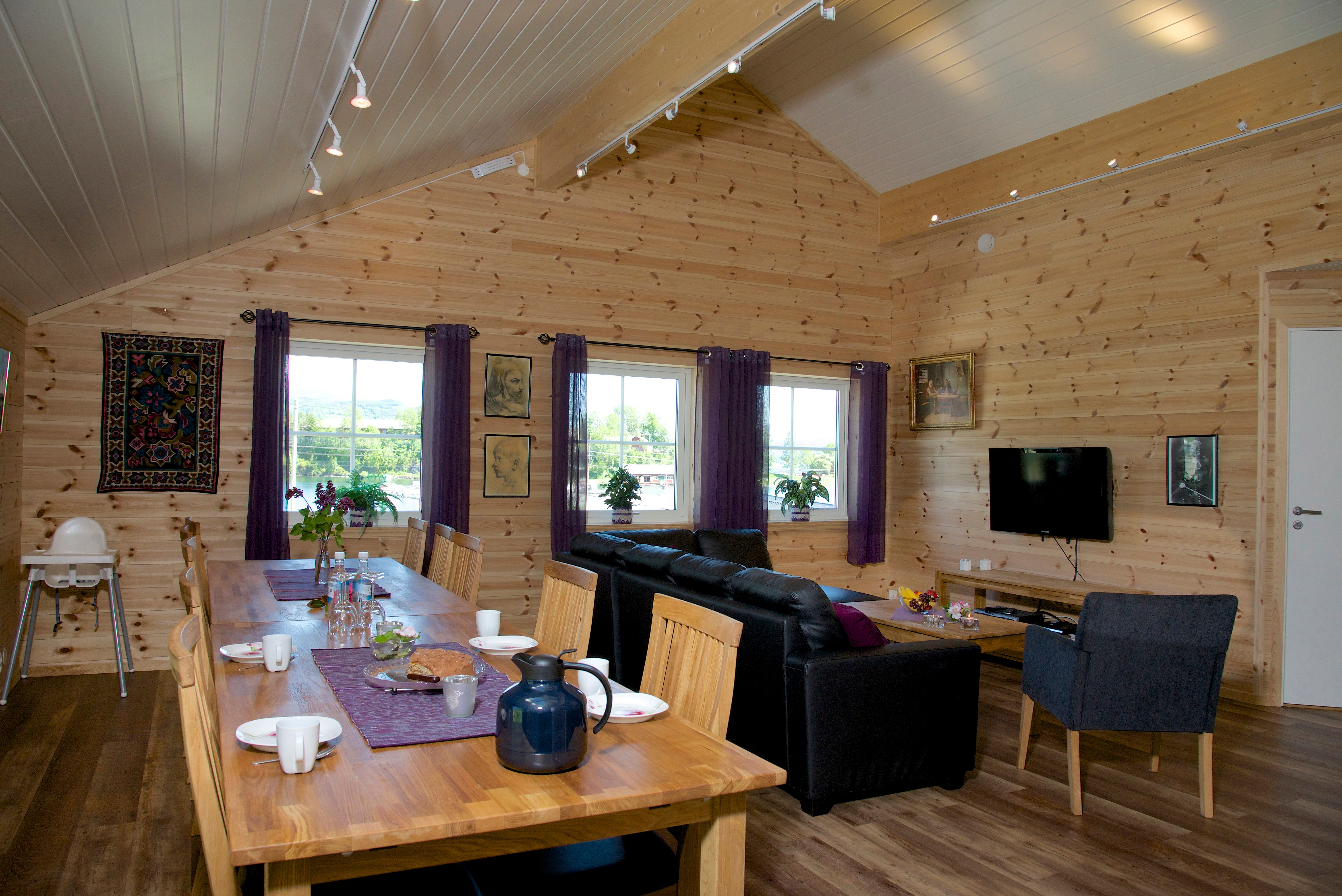 Cozy open living area with a long dining table, sofa lounge and TV at Vågen Rom og Hytteutleige in Hardanger.
