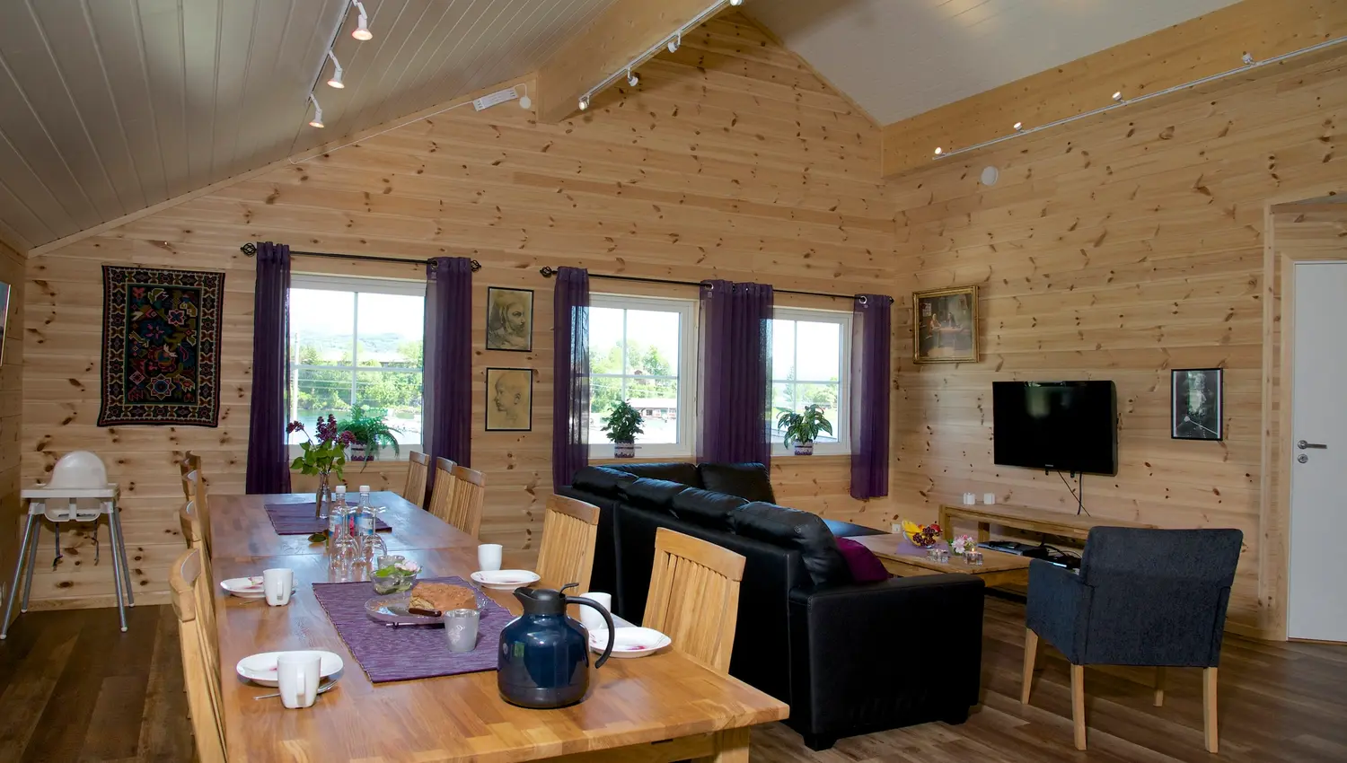 Cozy open living area with a long dining table, sofa lounge and TV at Vågen Rom og Hytteutleige in Hardanger.