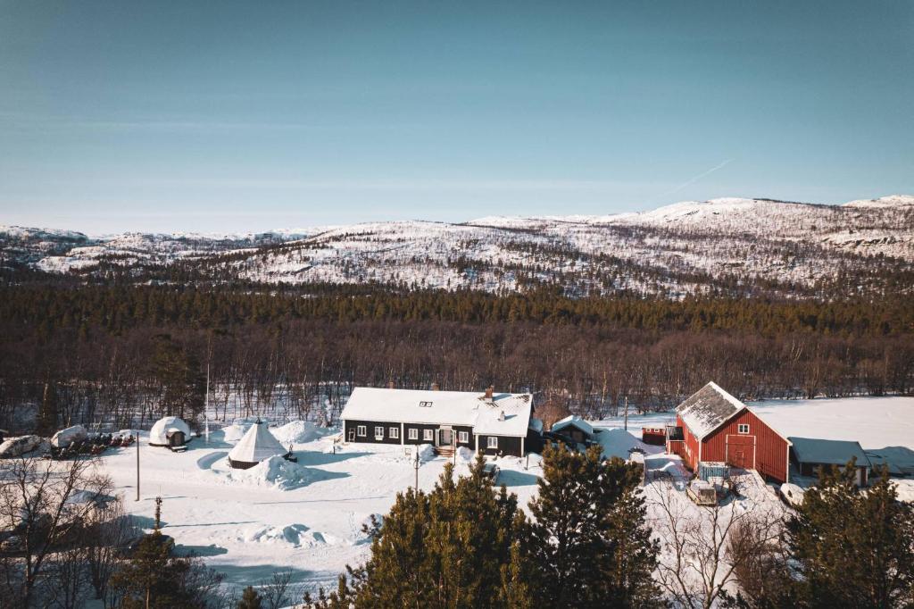 A snowy landscape featuring wooden cabins and mountains in the background.