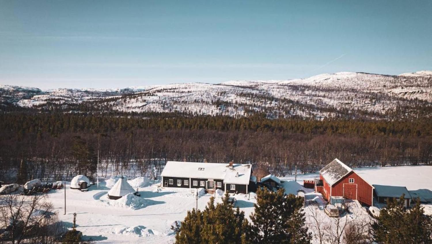 A snowy landscape featuring wooden cabins and mountains in the background.