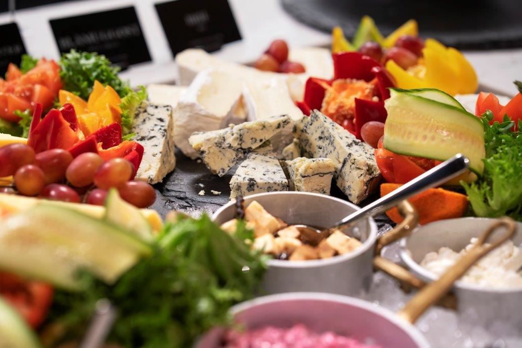 Cheese platter with various cheeses, fruit, vegetables, and small bowls of accompaniments.