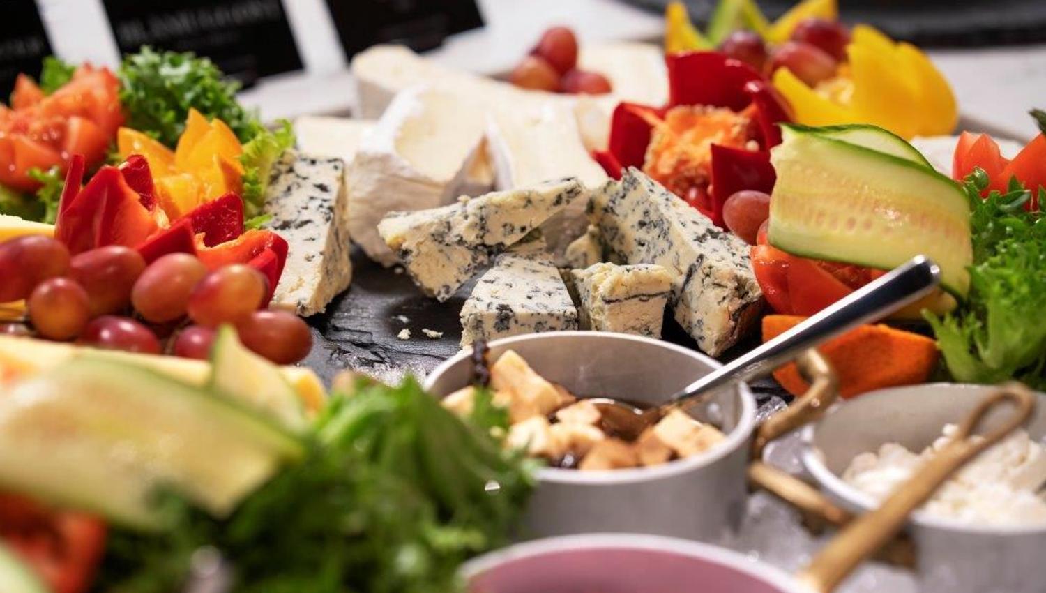 Cheese platter with various cheeses, fruit, vegetables, and small bowls of accompaniments.