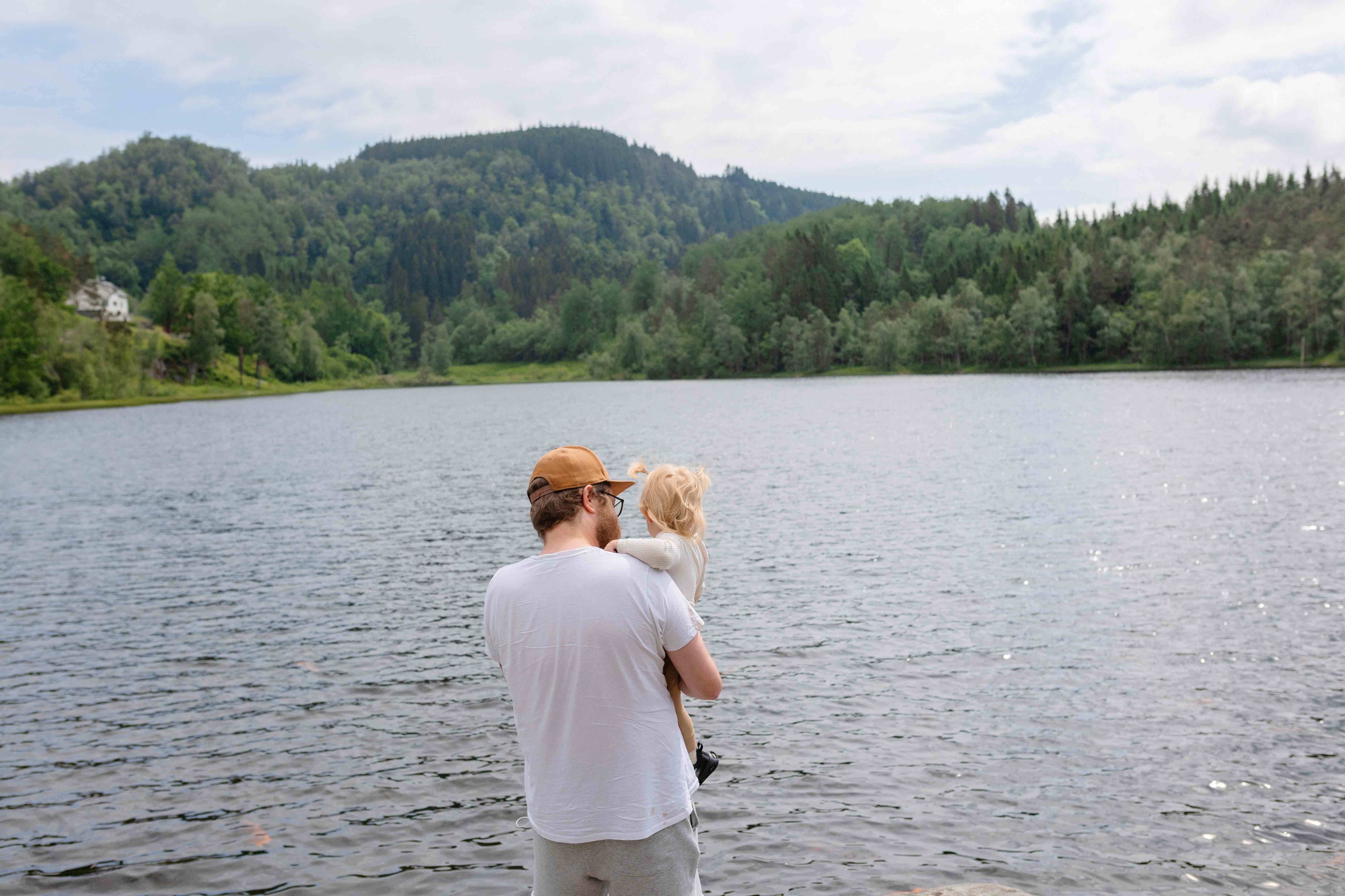 Ein vaksen held eit lite barn i armane sine medan dei ser utover Gullfiskvatnet og den vakre naturen rundt.
