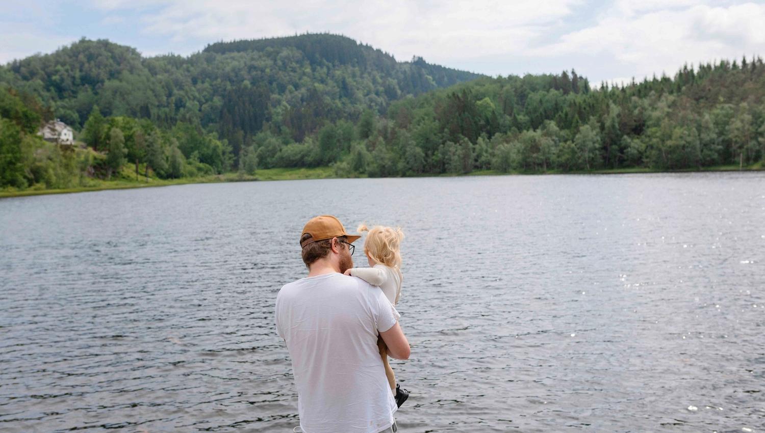 Ein vaksen held eit lite barn i armane sine medan dei ser utover Gullfiskvatnet og den vakre naturen rundt.
