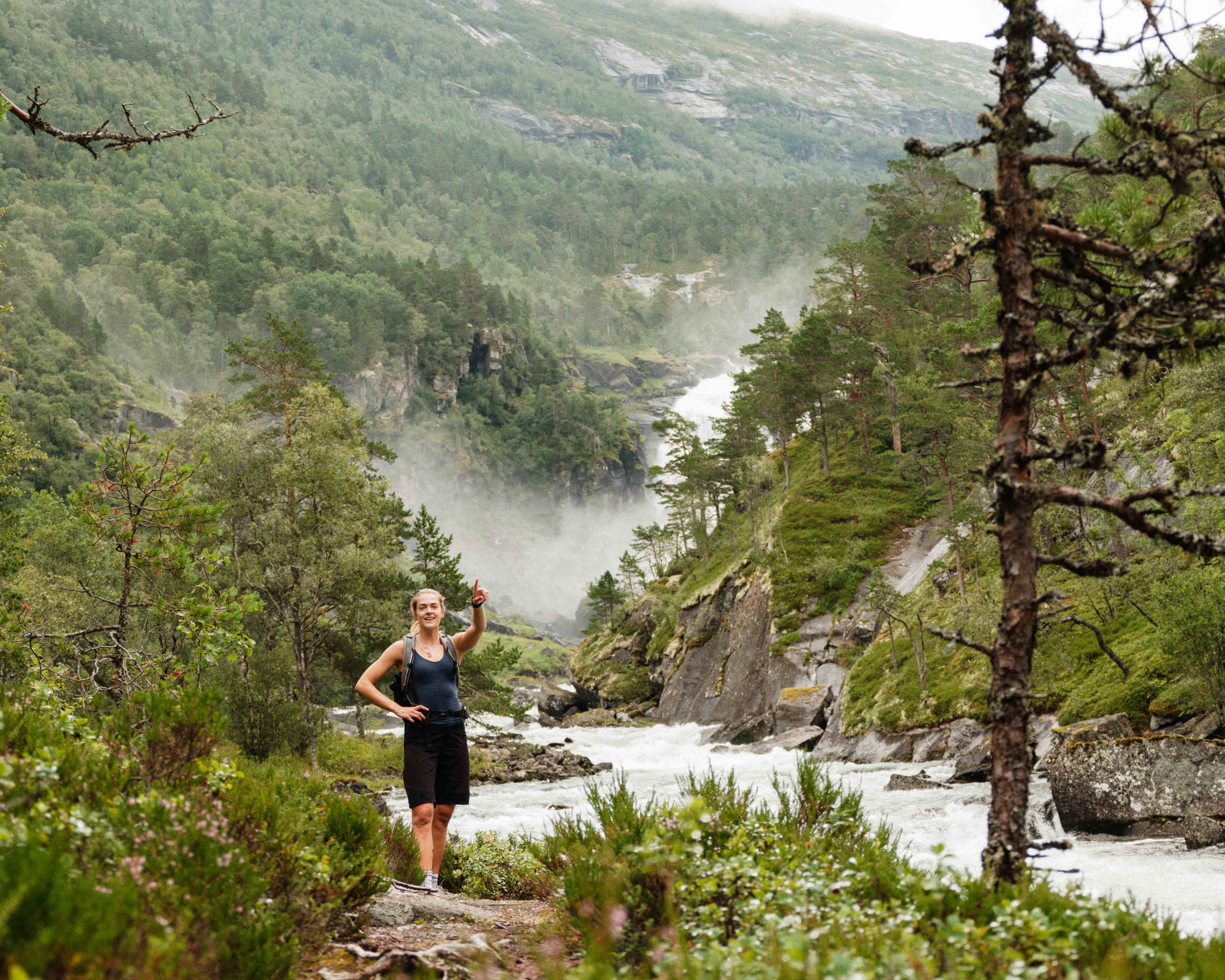 Hiker pointing towards distant waterfalls – Husedalen offers dramatic natural experiences.
