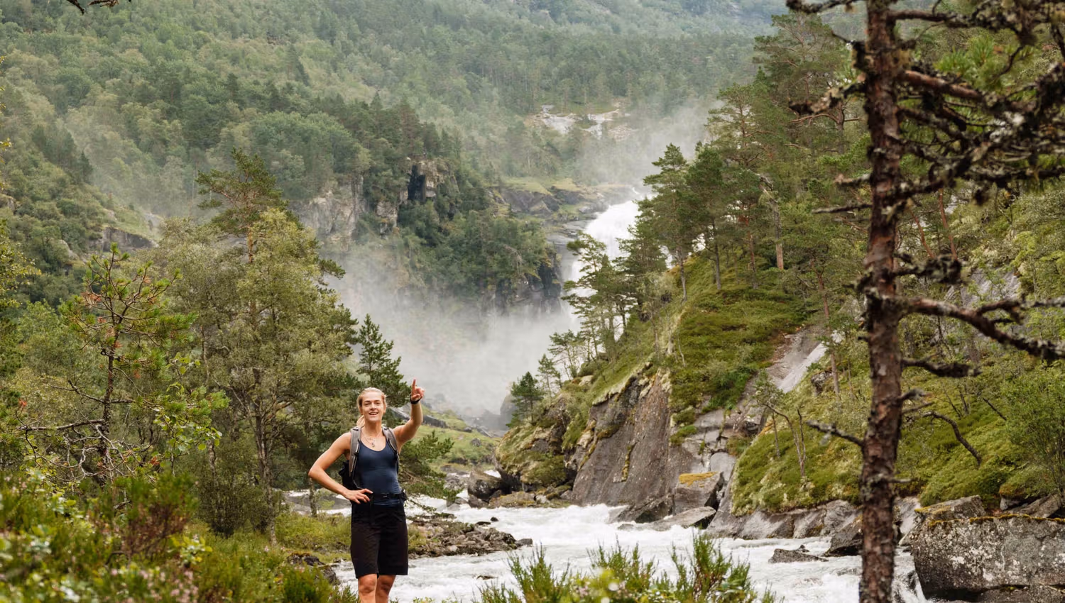 Hiker pointing towards distant waterfalls – Husedalen offers dramatic natural experiences.