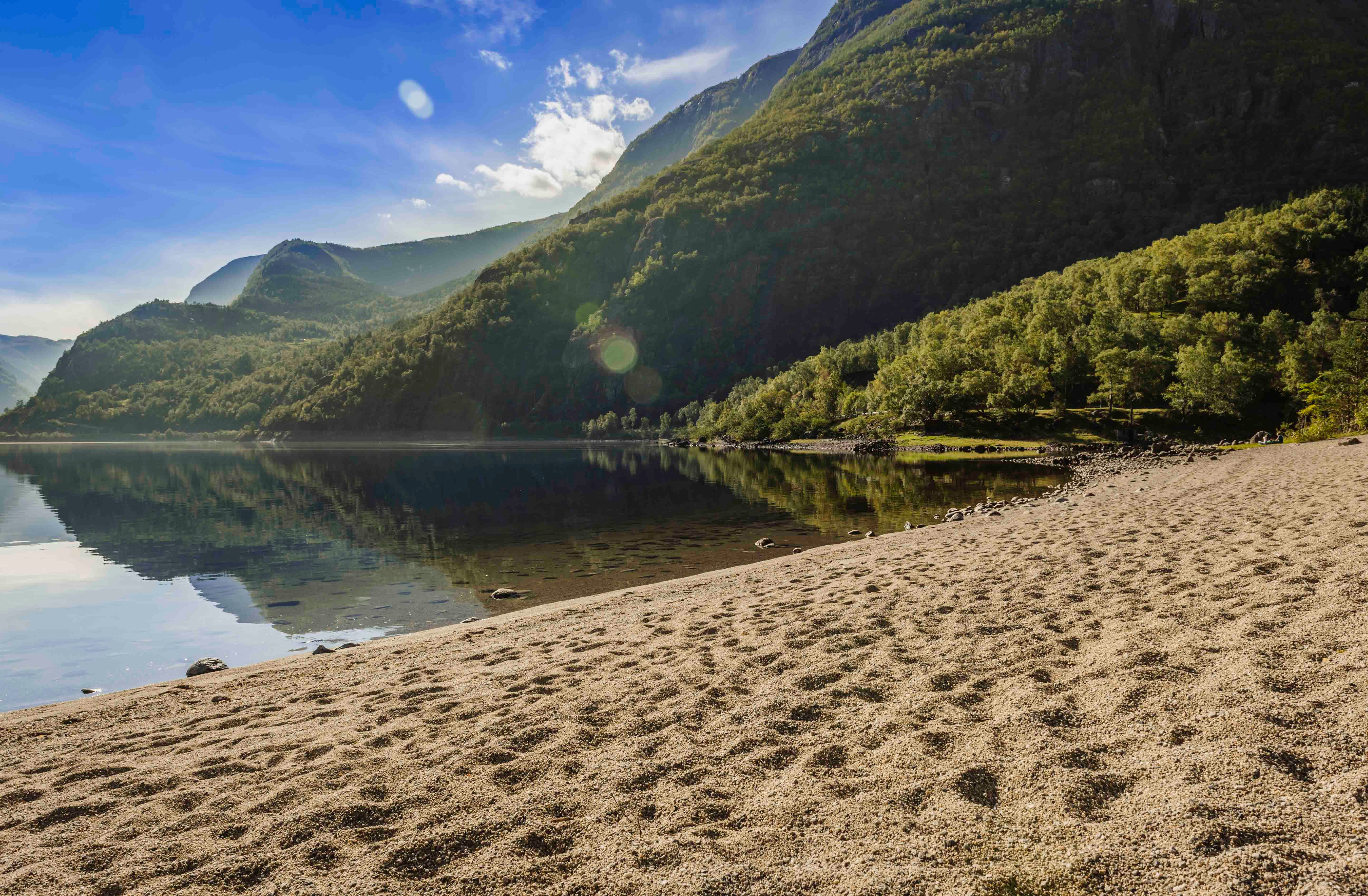 The sandy beach by the Eidfjord lake. The mountains surrounding the lake is reflecting perfectly in the lake.