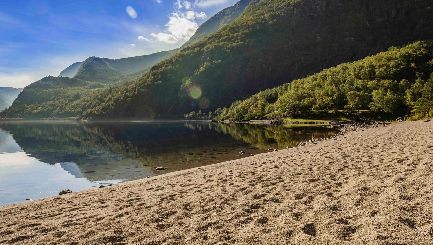 The sandy beach by the Eidfjord lake. The mountains surrounding the lake is reflecting perfectly in the lake.