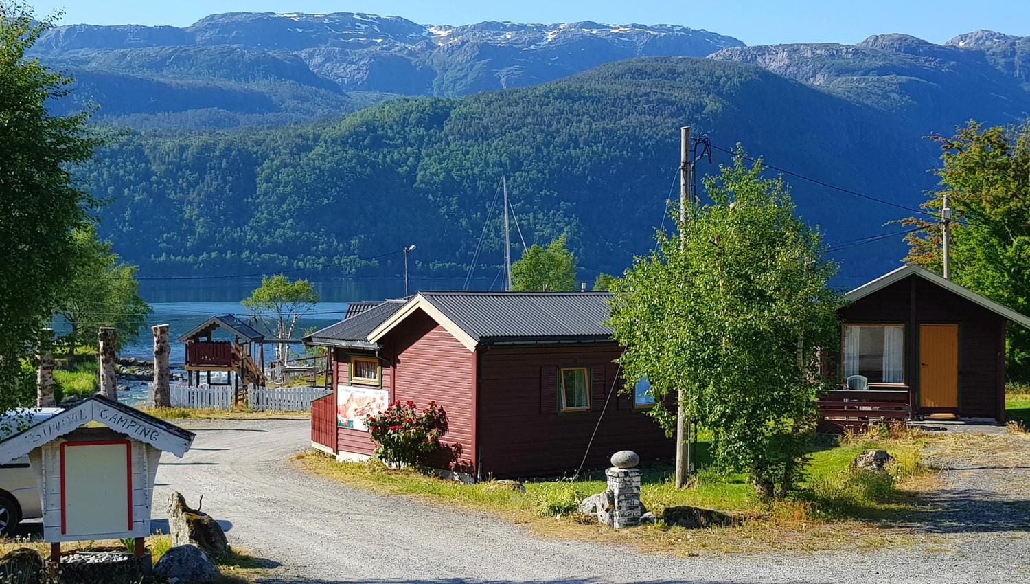 Innkøyring til campingplassen med velkomstpreg og fjordlandskap i bakgrunnen.