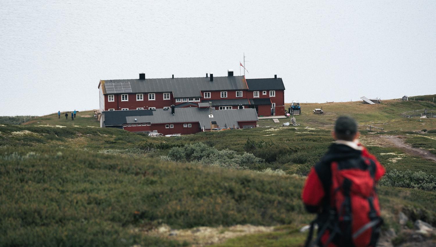 A hiker standing on top of a hill looking down towards the rauhelleren mountain lodge.
