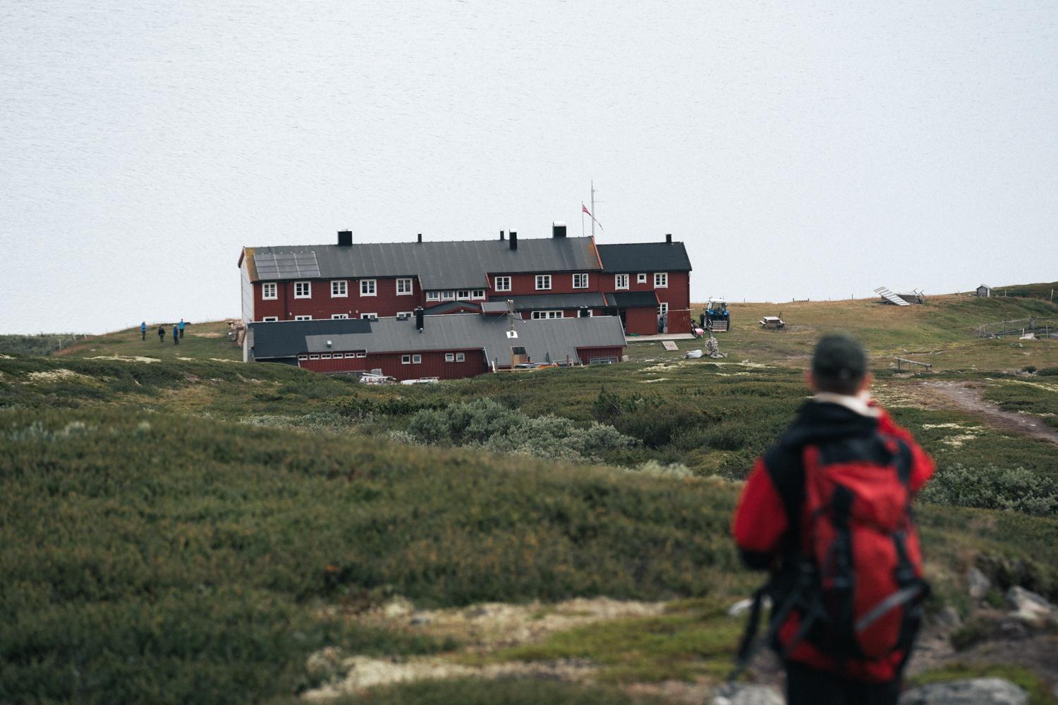 A hiker standing on top of a hill looking down towards the rauhelleren mountain lodge.