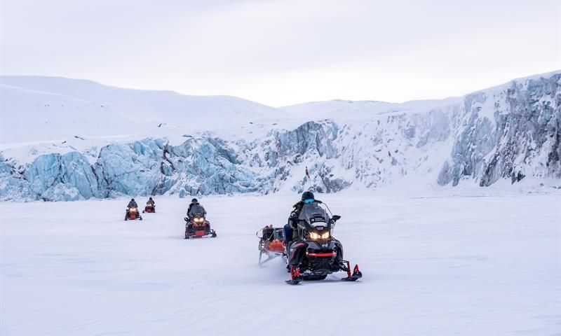 Snøscootere kjører over åpent snølandskap.