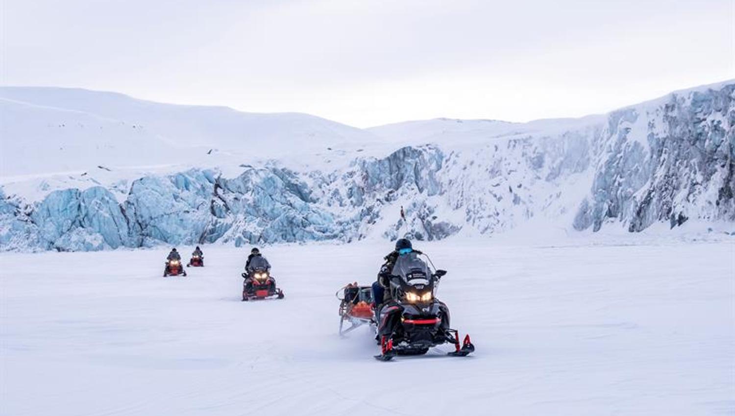 Snøscootere kjører over åpent snølandskap.